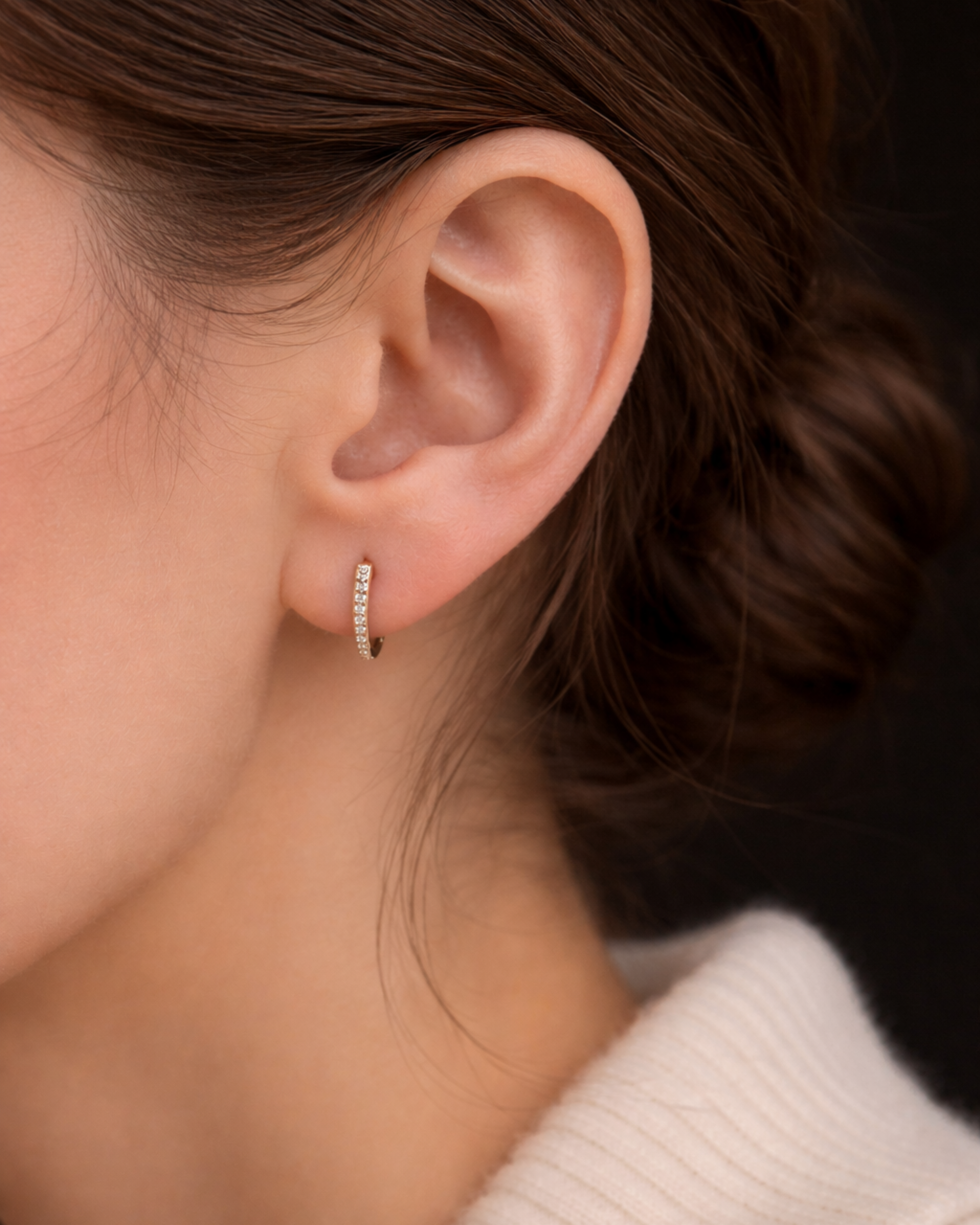 A woman wearing the Modernist Graduating Pave Hoop, a small gold earring with sparkling pave stones.