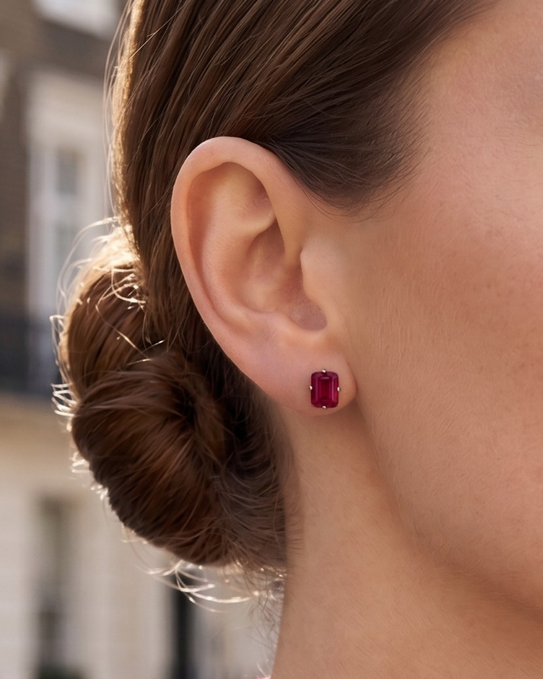 A close-up of a model's ear, wearing an emerald-cut ruby stud earring from the Lark & Berry London Bridge collection.