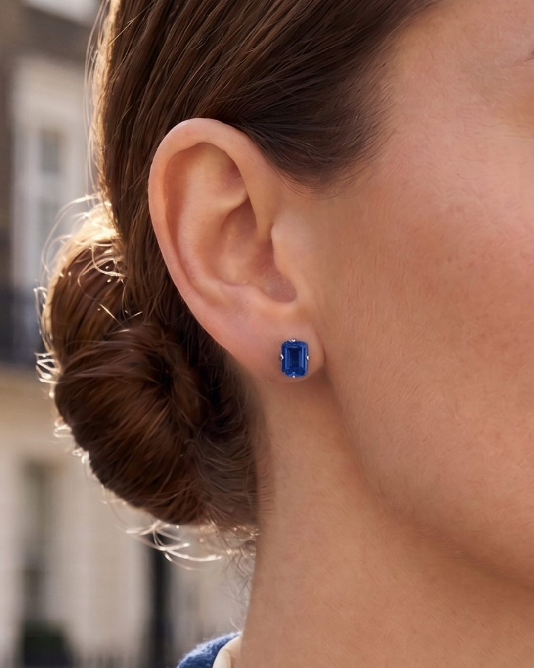 A woman wears a Lark & Berry London Bridge Blue Sapphire Stud earring with a bright, emerald-cut stone.