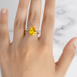 A hand models the Flora Oval Yellow Sapphire Cocktail Ring, showing its brilliant faceted stone and gold band on a marble surface.
