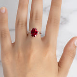 A woman's hand modeling the Flora Oval Ruby Cocktail Ring with diamond accents in 18k white gold against a marble surface.