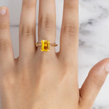 A model's hand wearing the Flora Yellow Sapphire Octad Cocktail Ring with a gold band against a white marble background.