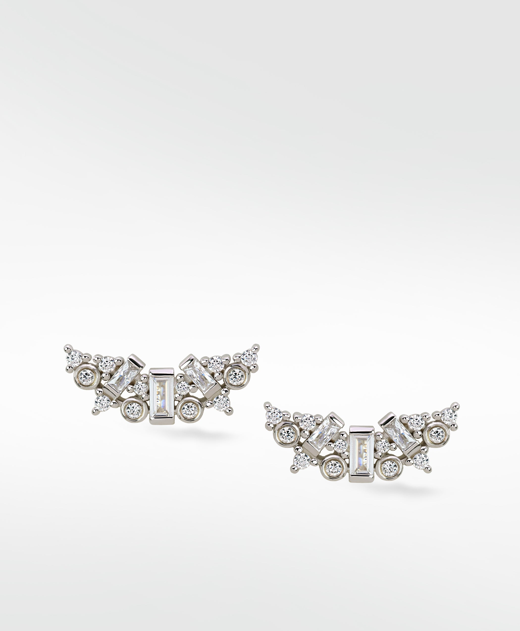 A pair of Lark & Berry Dove Duet white gold earrings with a cluster of baguette and round diamonds in a curved wing design.