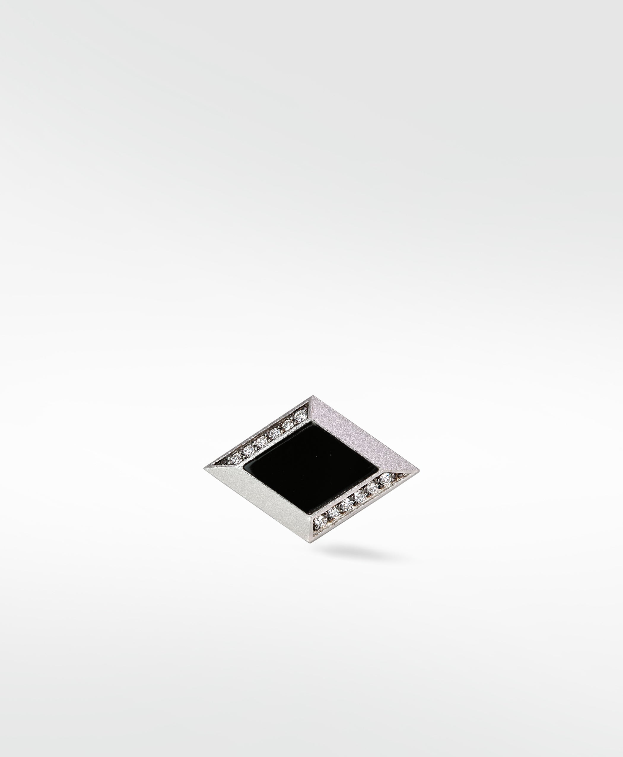 A single Clarke cufflink in matte silver, shaped like a diamond with a black center and pavé diamond accents.