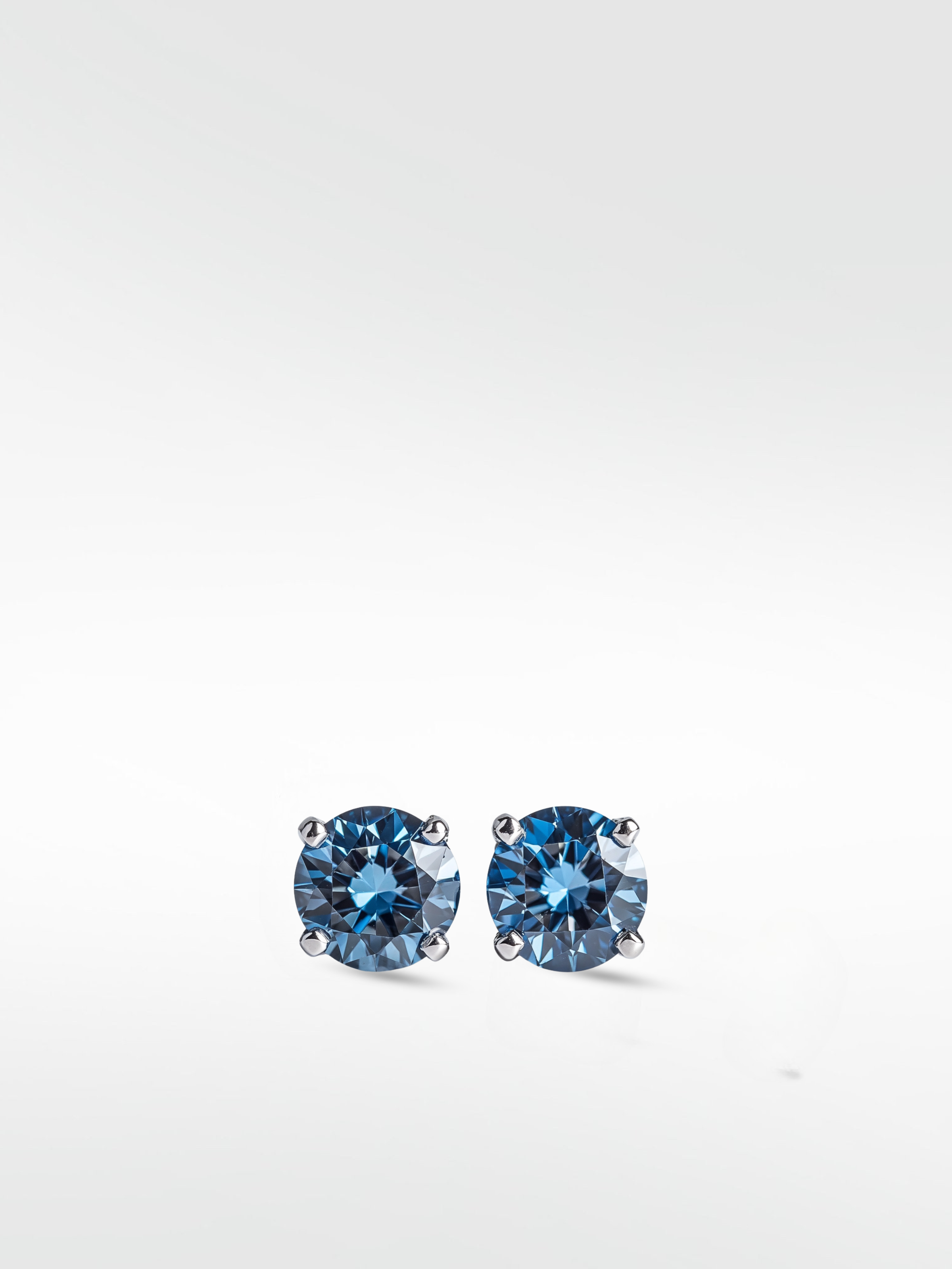 Pair of brilliant round-cut lime blue diamond stud earrings in a silver-toned four-prong setting.