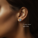 Close-up on a model's ear wearing a 2 carat, brilliant round cut, light blue diamond stud earring.