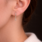 Model's ear showcases the Modernist Celestial Drop Hoop, a gold earring with a delicate, sparkling diamond drop.