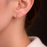 Model's ear showcases the Modernist Celestial Drop Hoop, a gold earring with a delicate, sparkling diamond drop.