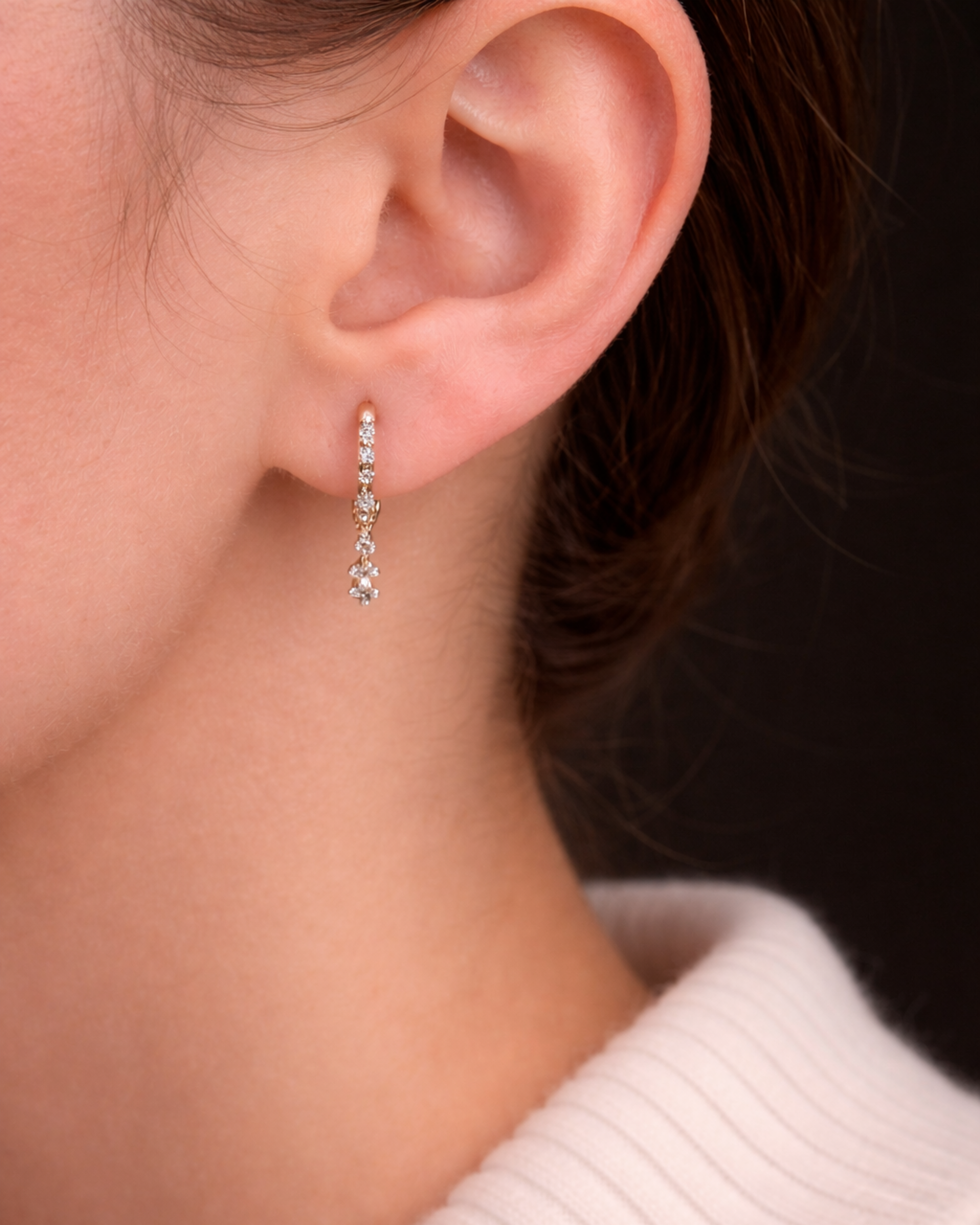 Model's ear showcases the Modernist Celestial Drop Hoop, a gold earring with a delicate, sparkling diamond drop.