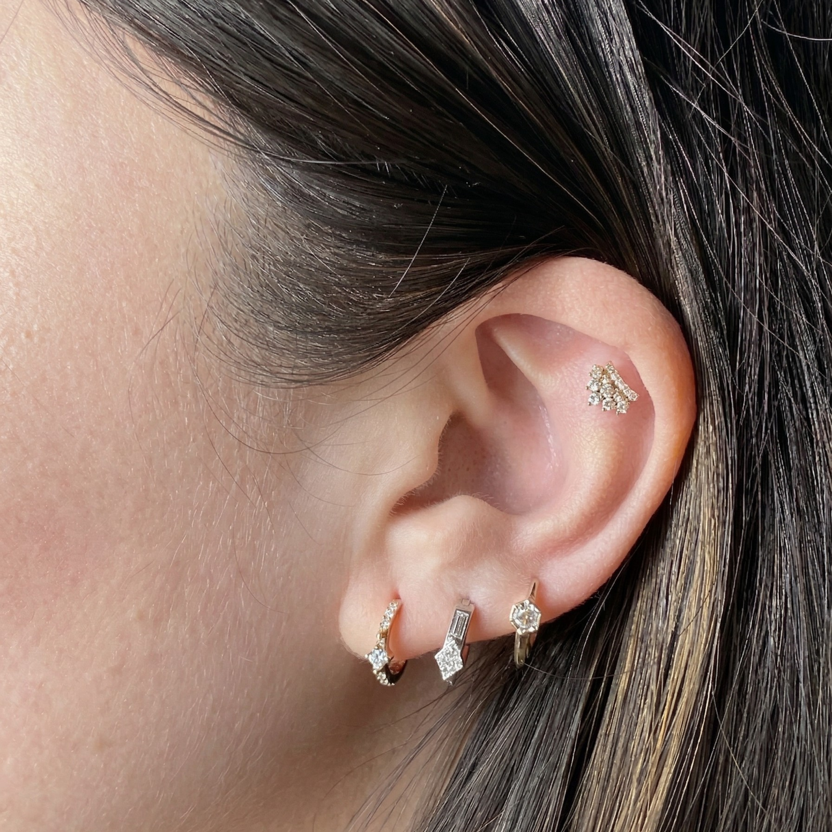 A model's ear with a curated stack featuring the Modernist Triangle and Baguette Diamond Hoop, styled with other diamond earrings.