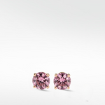 A pair of brilliant round-cut pink diamond stud earrings in a classic four-prong gold setting, shown on a white background.