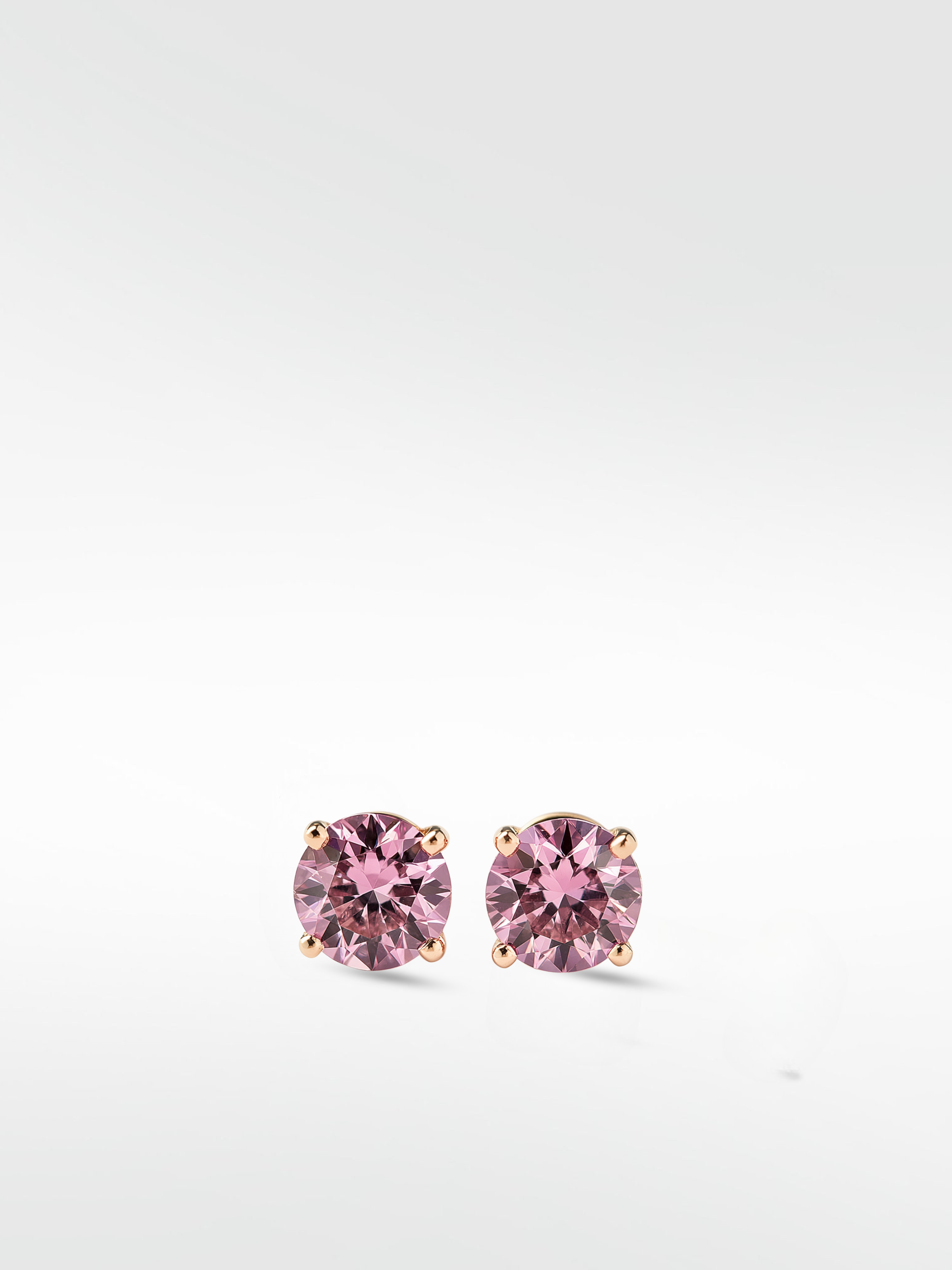 A pair of brilliant round-cut pink diamond stud earrings in a classic four-prong gold setting, shown on a white background.