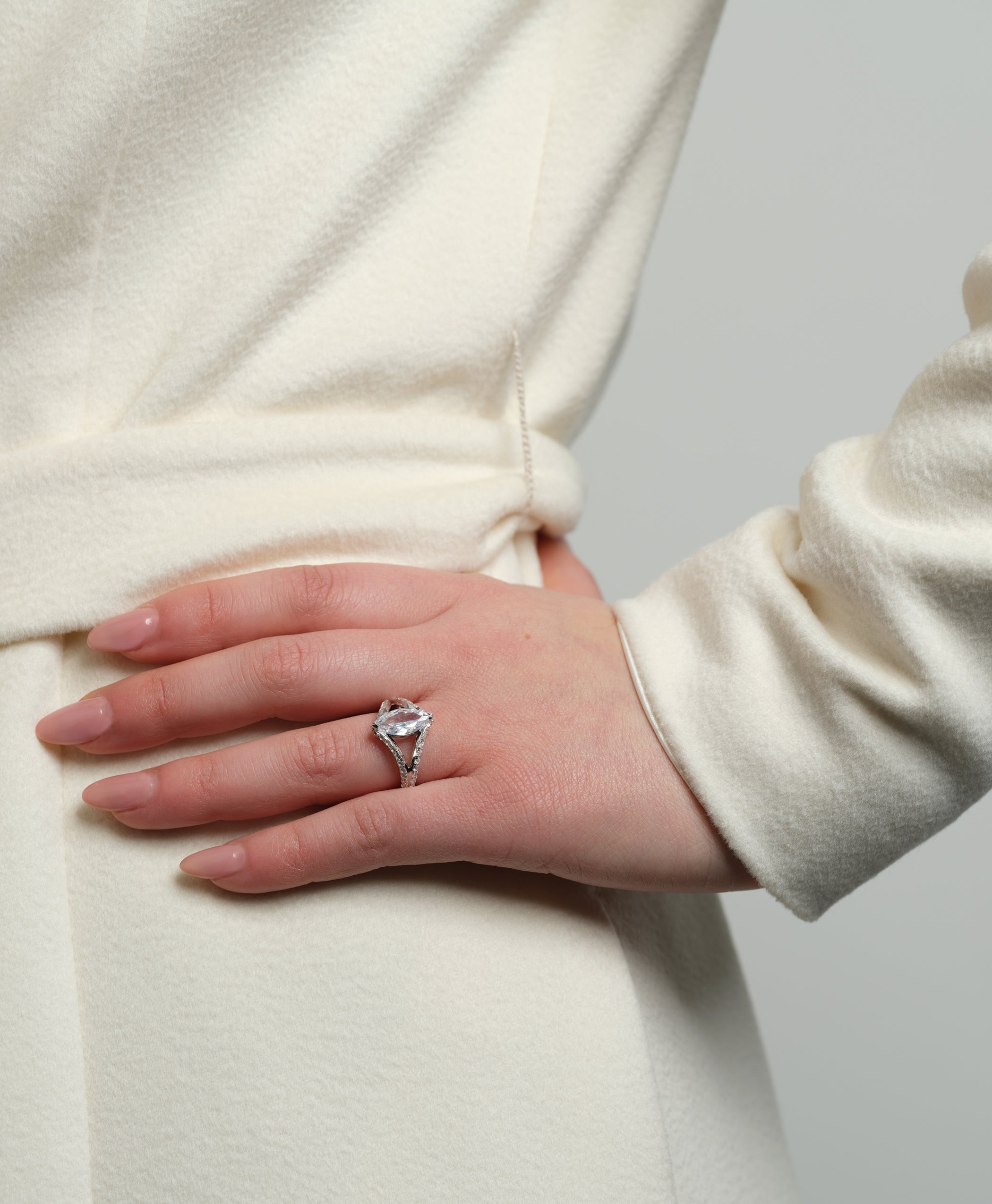 A model's hand with the Chestnut Diamond Engagement Ring, featuring a marquise-cut stone, resting on a cream coat.