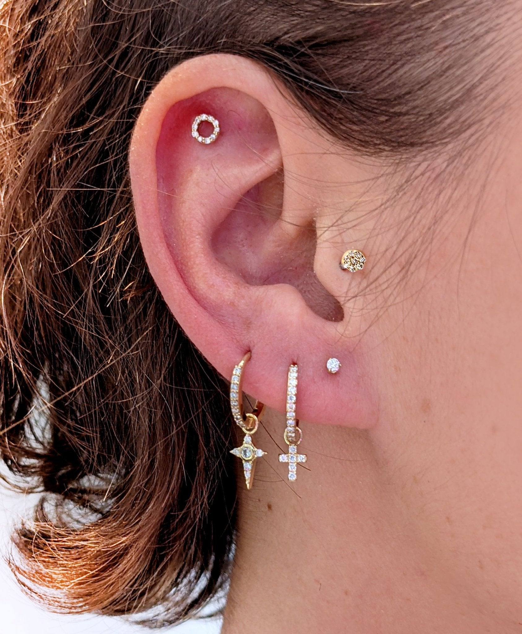 Close-up of a curated ear featuring a gold Celestial Diamond star charm on a hoop, styled with other diamond earrings and studs.