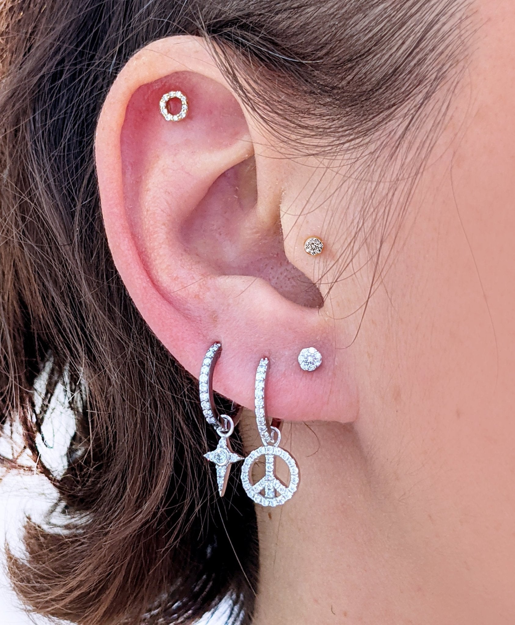 A close-up of an ear styled with a Celestial Diamond Charm on a silver hoop, paired with other diamond earrings and studs.
