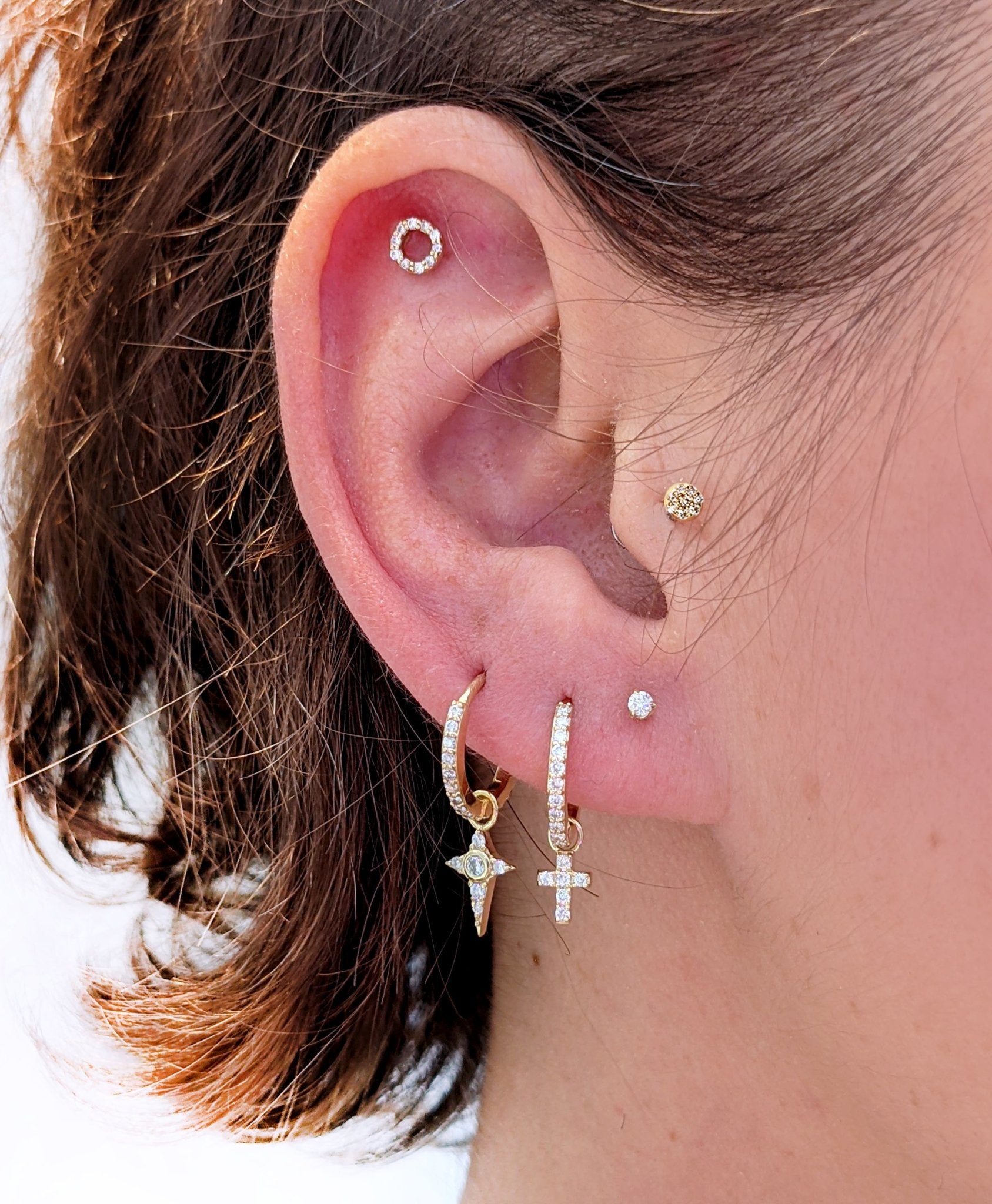 Close-up of a curated ear with Lark & Berry's gold Celestial Diamond star charm, a cross charm hoop, and various diamond studs.