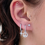 Close-up of a curated ear stack with a diamond celestial star charm on a hoop, next to a peace sign charm and other diamond studs.
