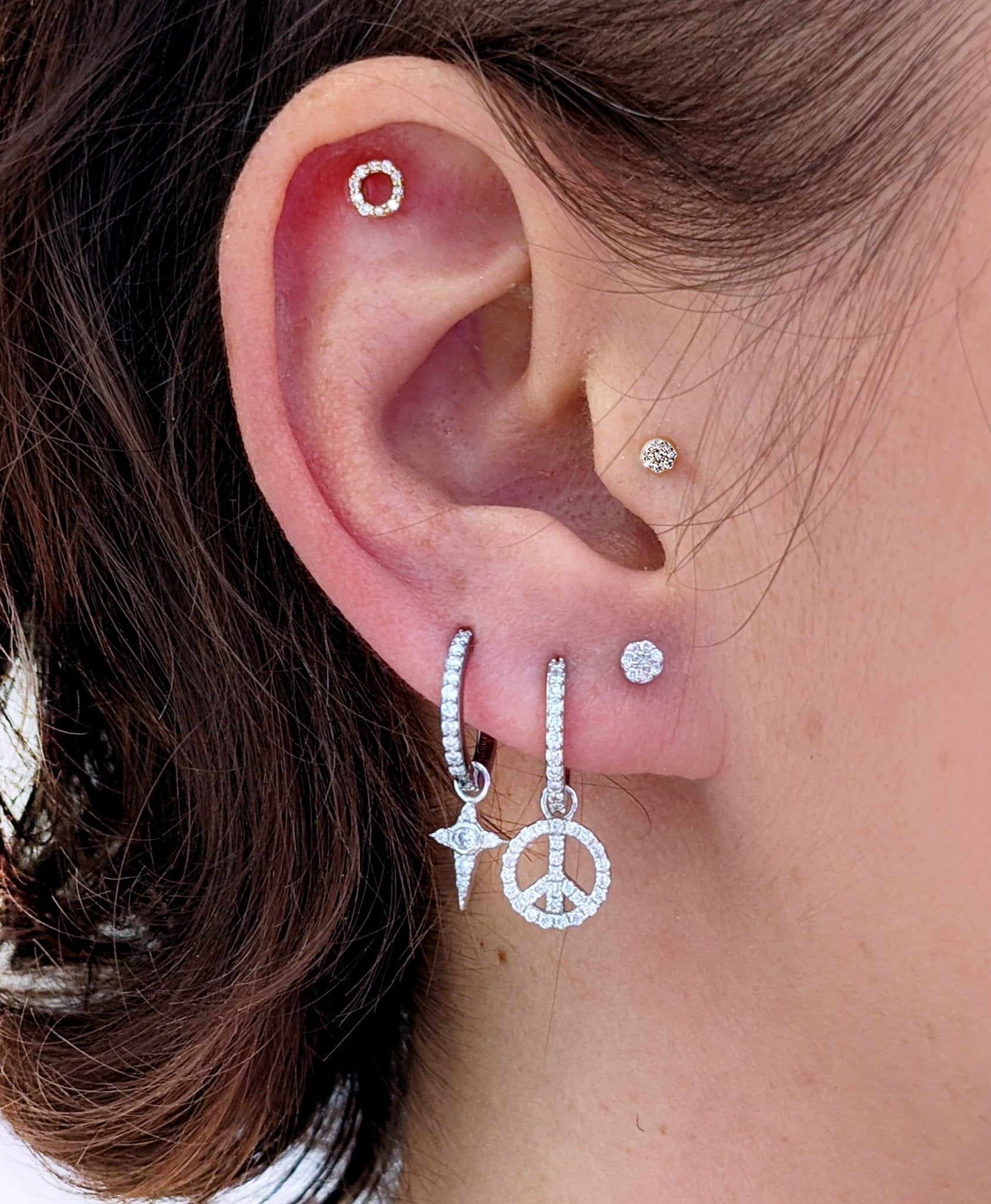 Close-up of a curated ear stack with a diamond celestial star charm on a hoop, next to a peace sign charm and other diamond studs.
